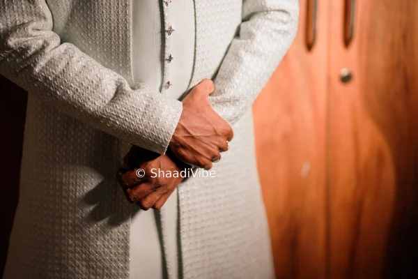 Elegant groom portrait featuring a confident Indian groom standing with his hands folded in a classic wedding pose.
