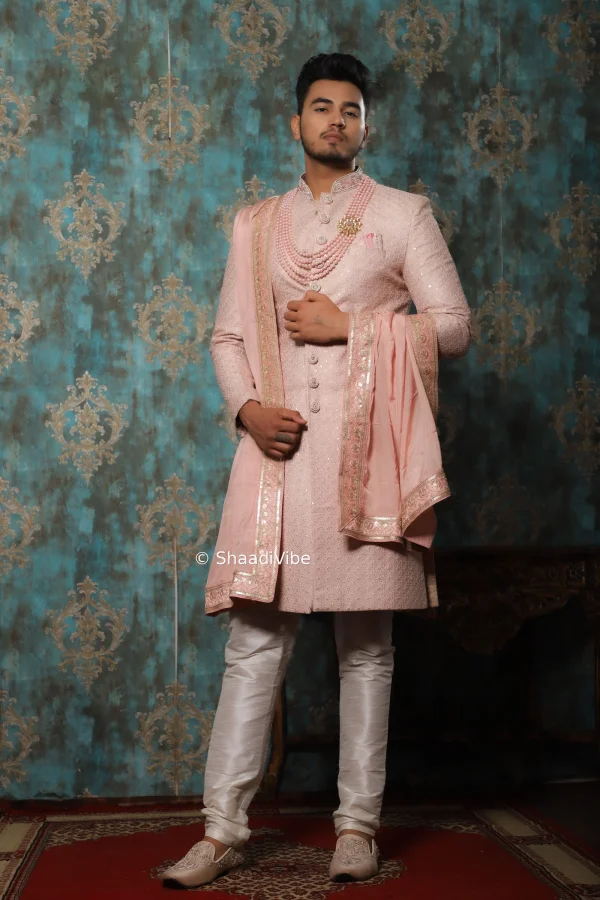 Royal pastel pink sherwani featuring with matching khesh with border on it and traditional styling for a grand Indian wedding ceremony.