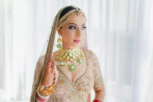 Traditional Indian bride posing in a detailed Off white lehenga with layered gold jewellery and a bridal dupatta.